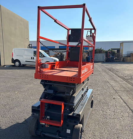 An orange scissor lift is parked in a parking lot