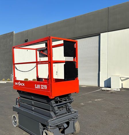 A red scissor lift is parked in front of a building