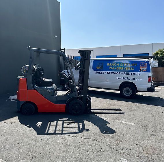 A forklift is parked in a parking lot next to a van.