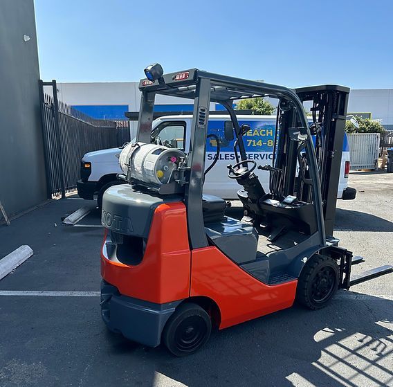 A forklift is parked in a parking lot next to a van that says ' a & a ' on it