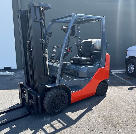 A red and black forklift is parked in front of a building
