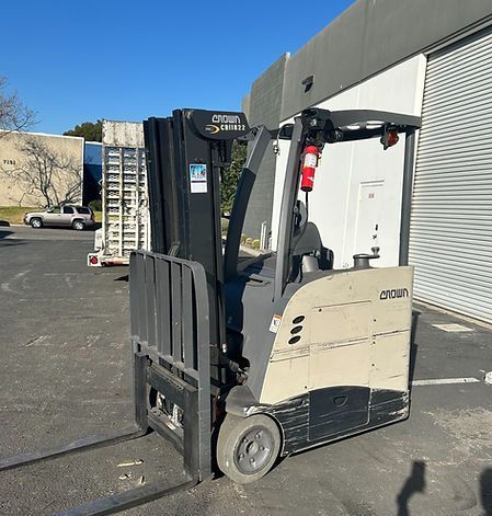 A forklift is parked in a parking lot in front of a building.