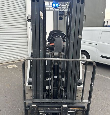 A forklift is parked in a parking lot next to a white van.
