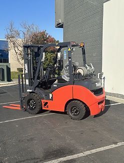 A red forklift is parked in a parking lot in front of a building.
