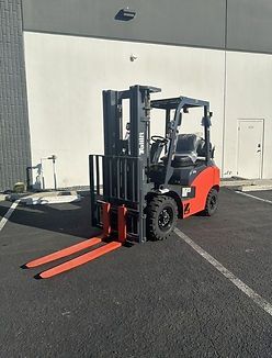 A forklift is parked in a parking lot in front of a building.