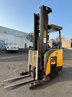A yellow and black forklift is parked in a parking lot in front of a building.