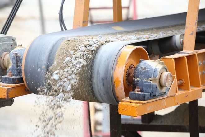 Conveyor belt carrying gravel, orange machinery, gray belt, material falling off, outdoor setting.