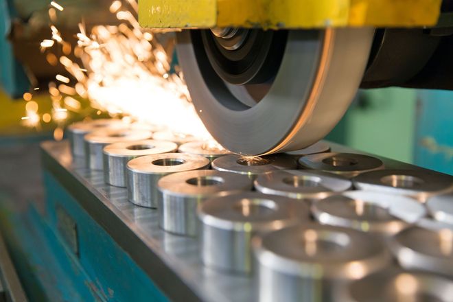 Metal grinder shaping metal rings, producing sparks in a factory setting.