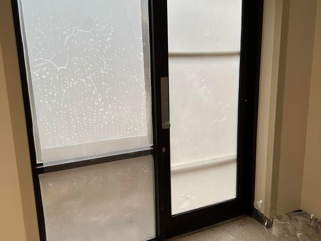 A black-framed door with frosted glass panes, showing condensation on the left side and a plain surface on the right.
