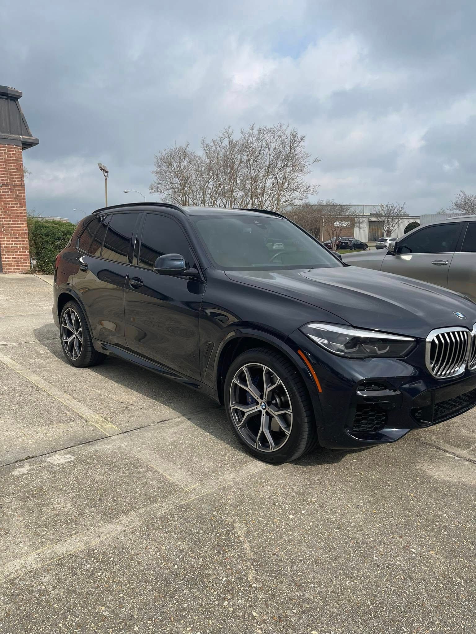 A black BMW SUV parked on a paved outdoor lot under a cloudy sky.