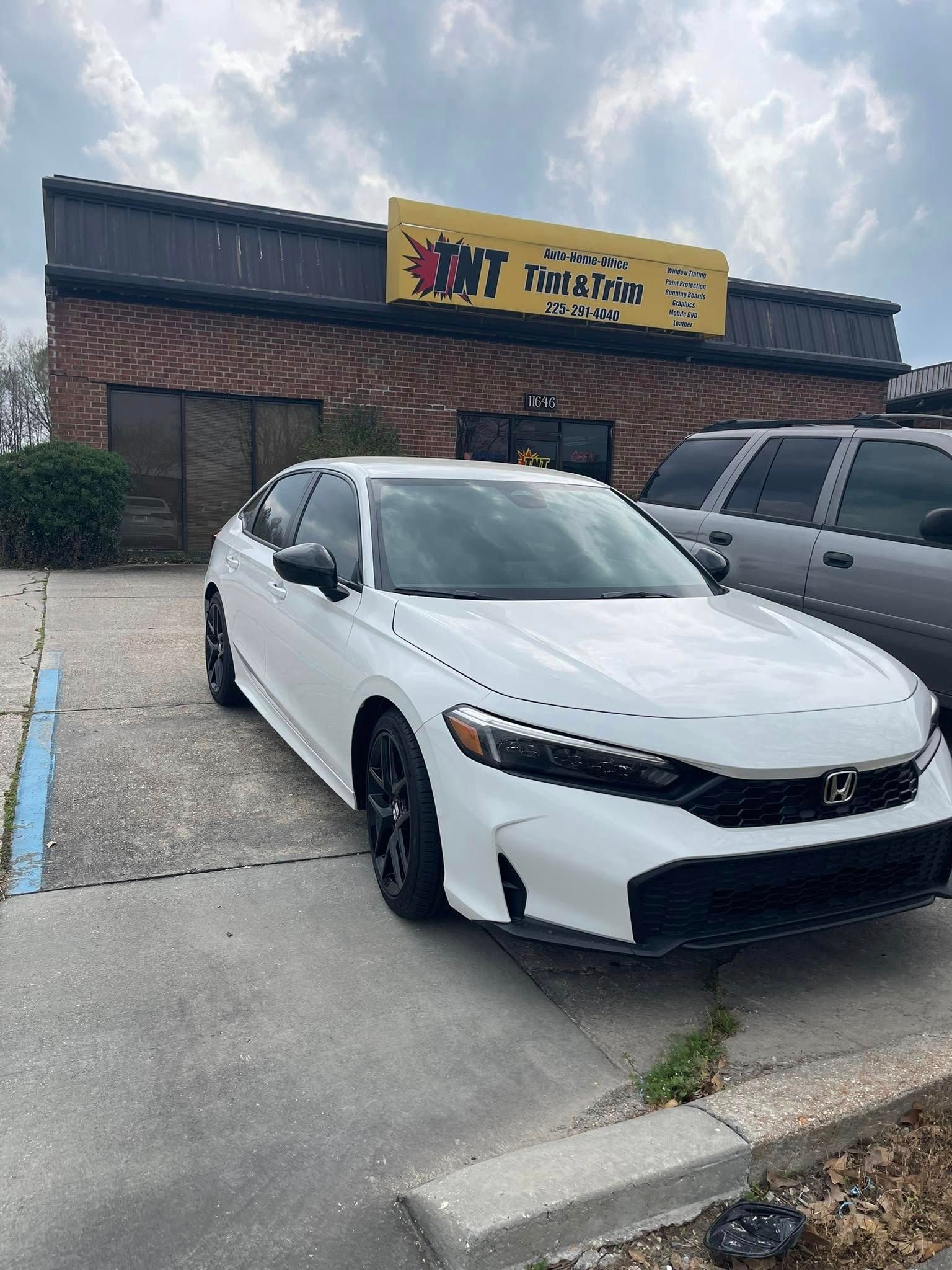 A white Honda sedan parked in front of a brick commercial building with a yellow TNT signage under a cloudy sky.