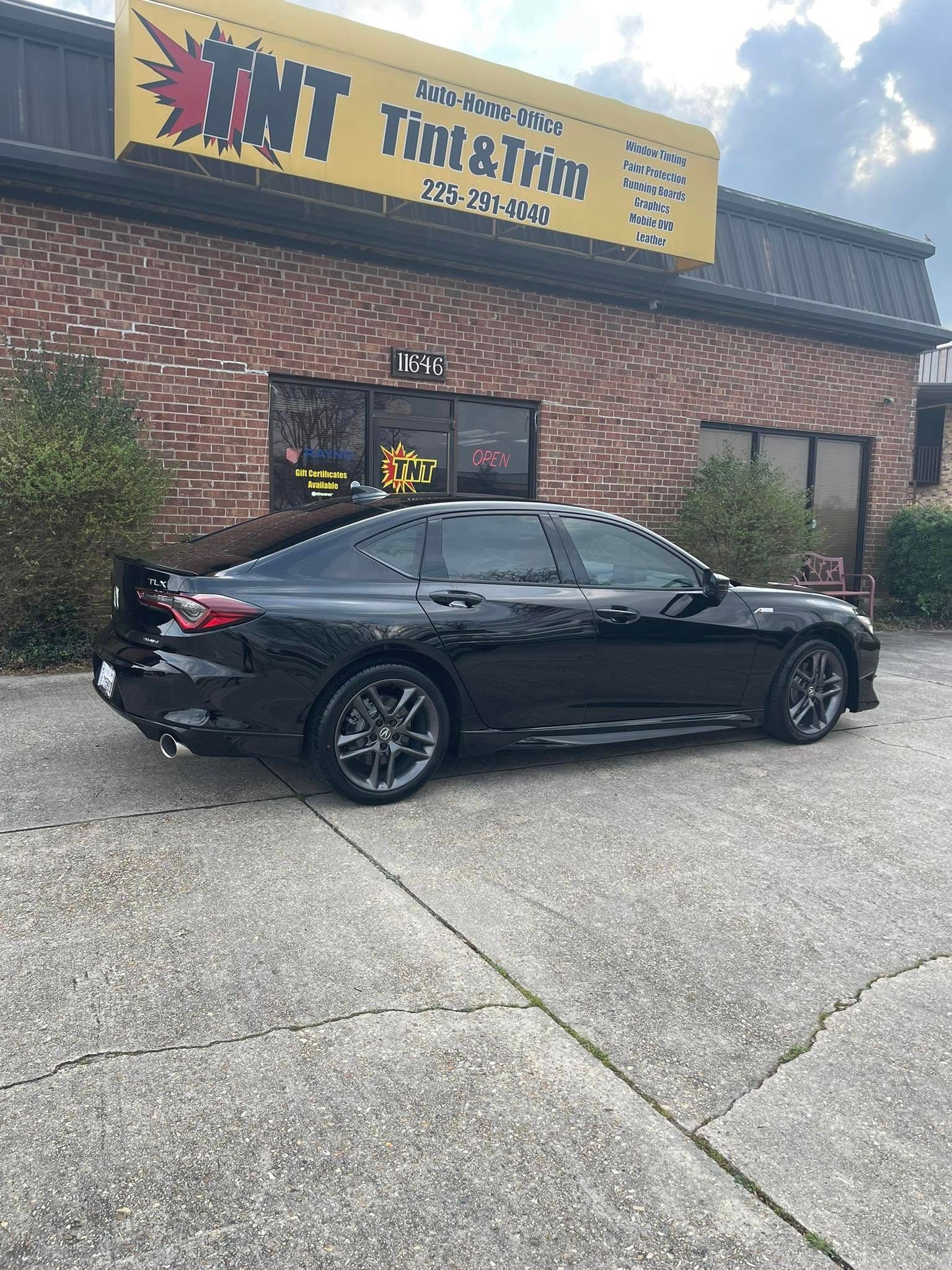 A black sedan parked in front of a brick building with a yellow sign that reads 