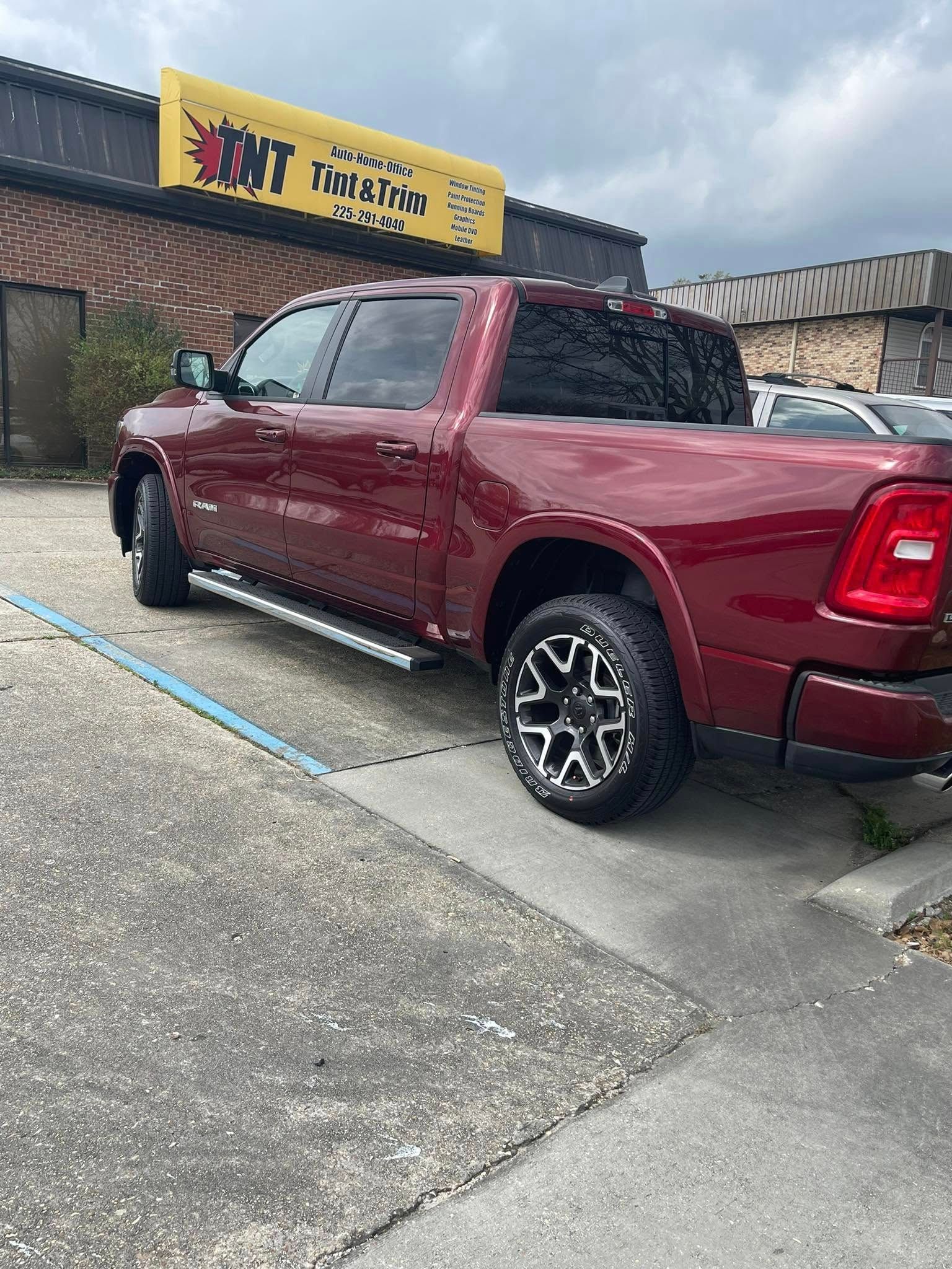 A maroon Ram pickup truck with custom black and silver wheels parked in front of a building with a yellow sign.