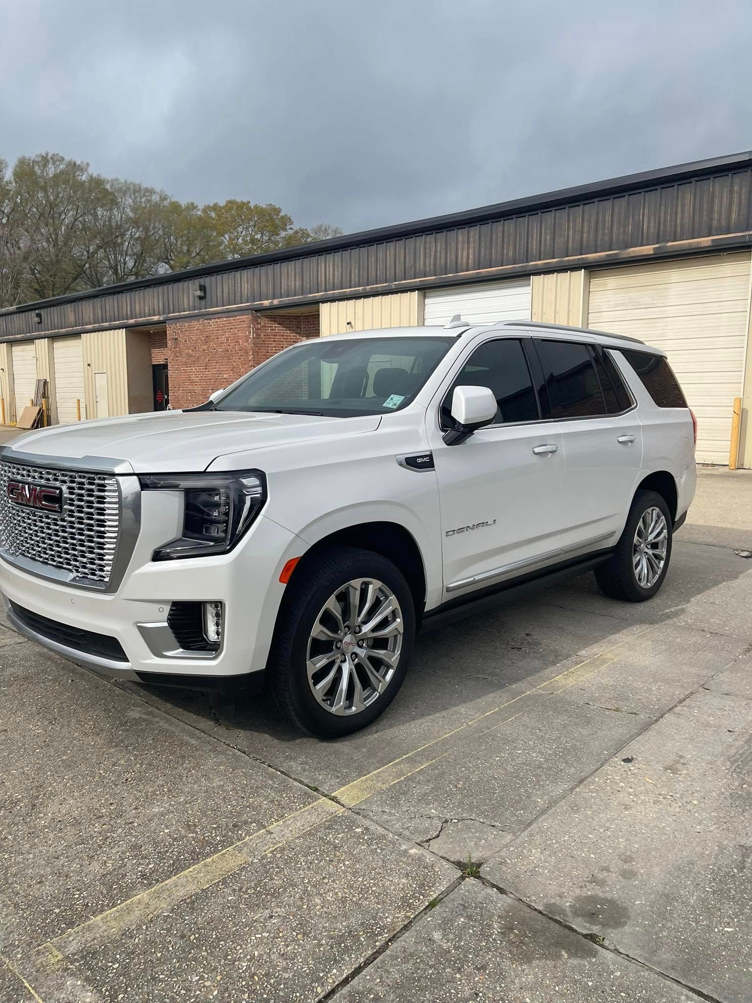 A white GMC Yukon Denali SUV parked on a paved lot in front of storage units.