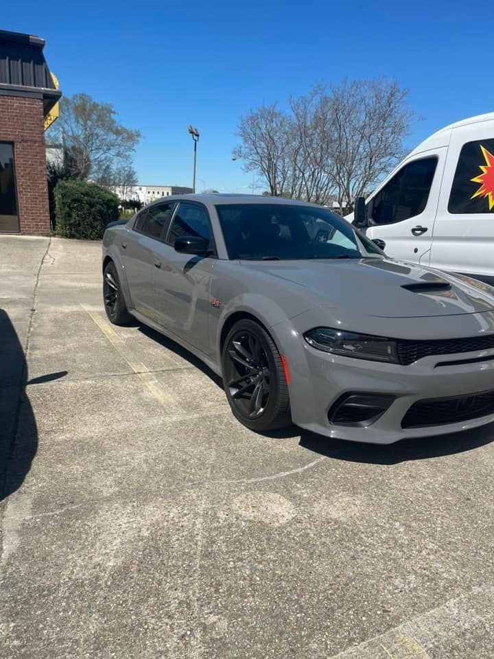 A gray Dodge Charger with a widebody kit parked on a paved lot on a sunny day next to a white work van.