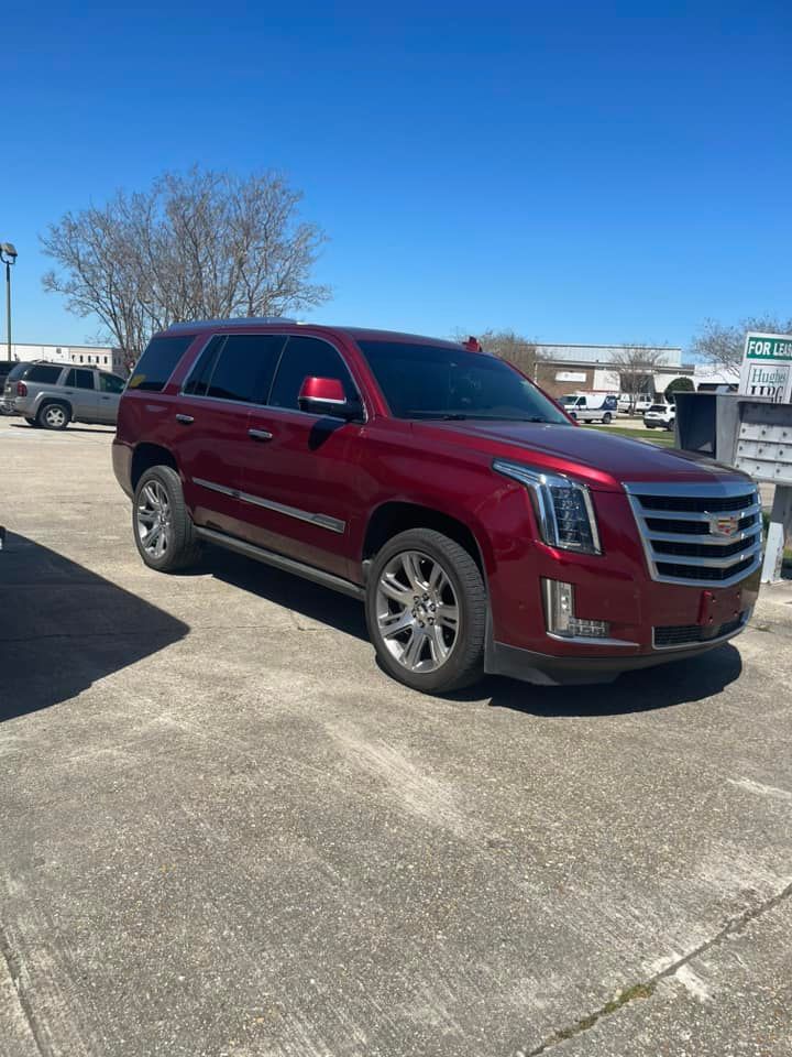 A maroon Cadillac Escalade SUV parked on a concrete lot under a clear blue sky.