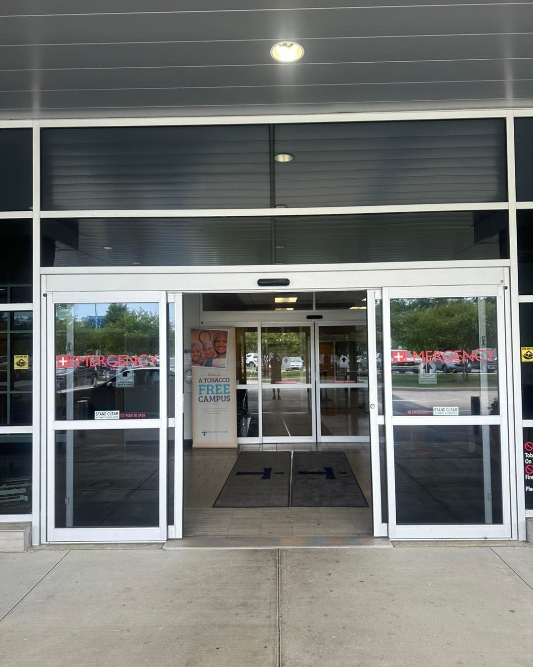 Automatic sliding glass doors at the entrance of a building, with a reflection of parked cars and trees visible outside.