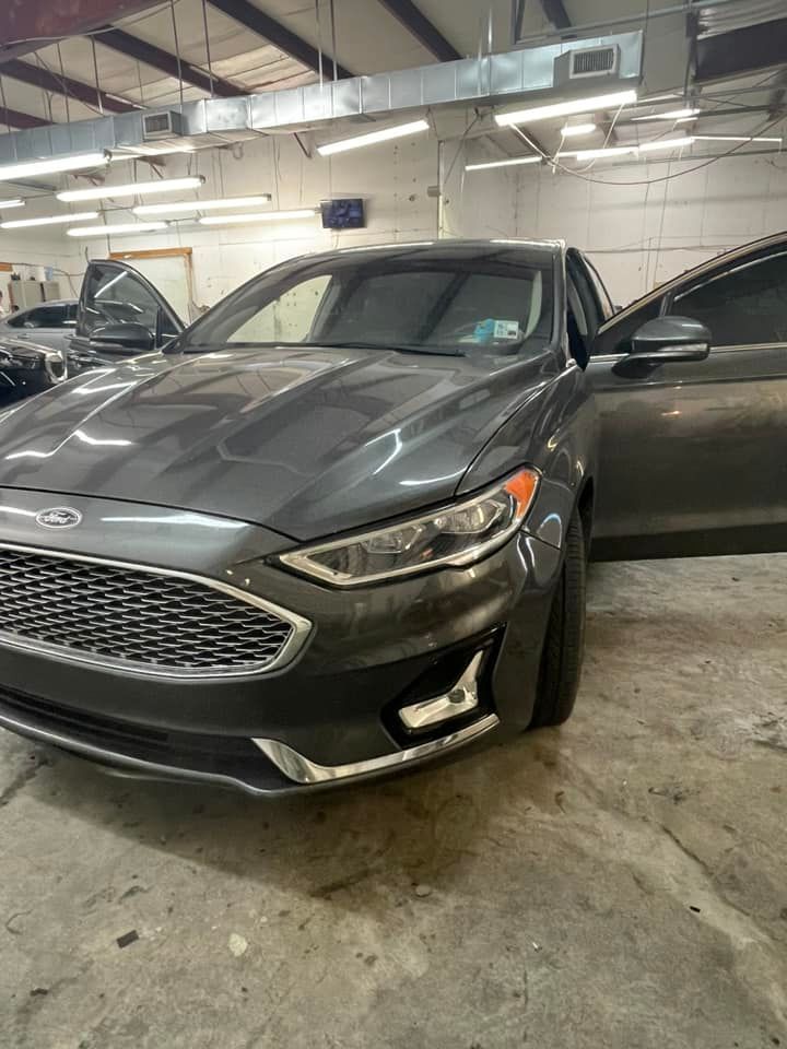 A grey Ford Fusion parked in a garage with its driver-side door open.