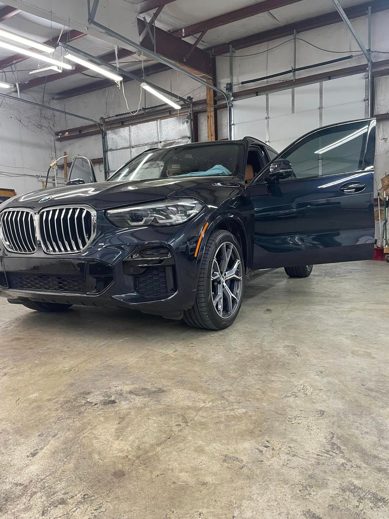 A dark-colored BMW SUV with its front door open, parked inside a garage with industrial lighting.