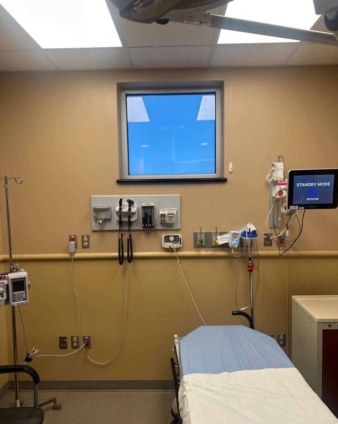 A hospital exam room with a medical bed, monitoring equipment, and wall-mounted diagnostic tools.