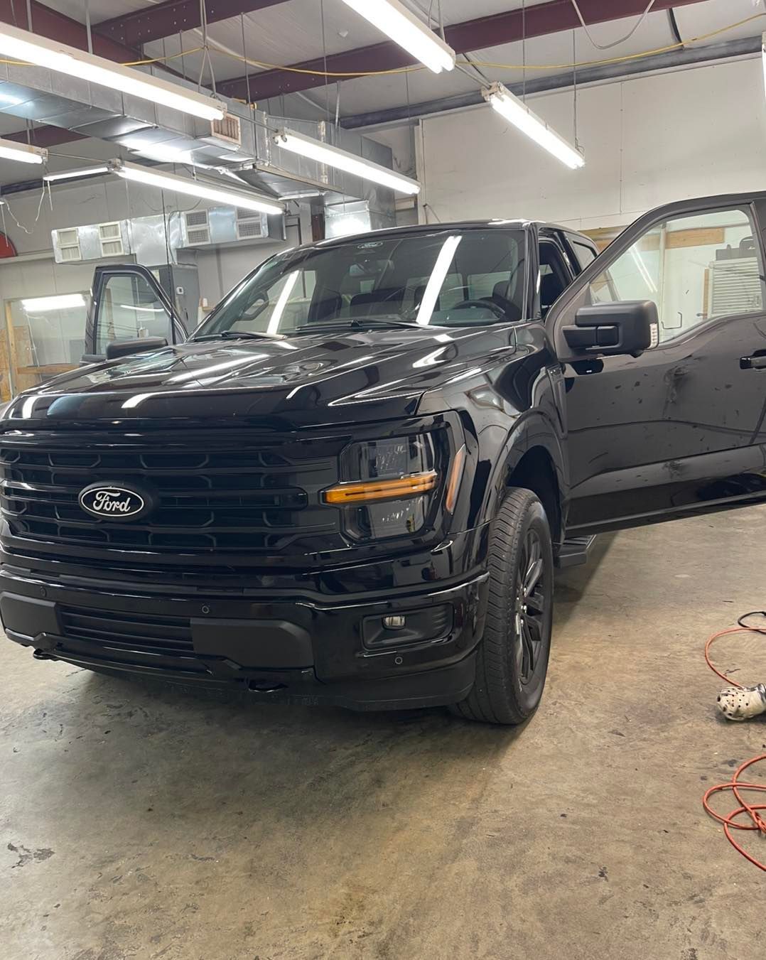 A black Ford pickup truck parked in a well-lit workshop with its driver-side door open.