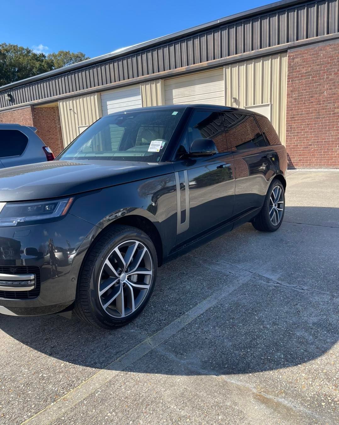 A black Land Rover Range Rover parked on a concrete lot in front of a building with roll-up doors.