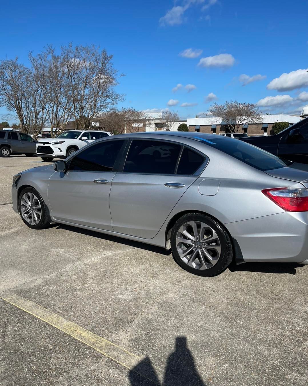A silver sedan parked in a sunlit, paved parking lot under a clear blue sky.