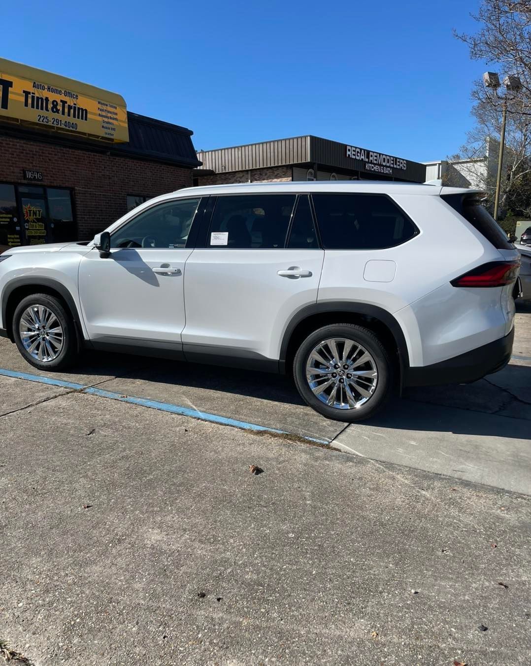 A white SUV parked in a paved lot in front of commercial buildings under a clear blue sky.
