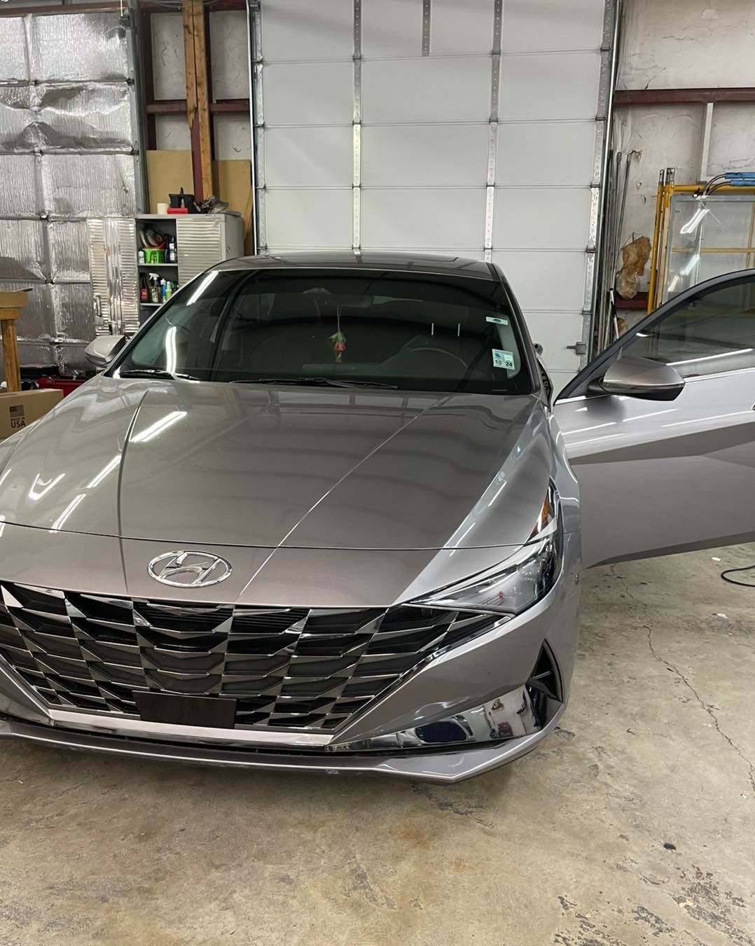 A grey Hyundai Elantra with an open driver’s side door parked inside an industrial-style shop.