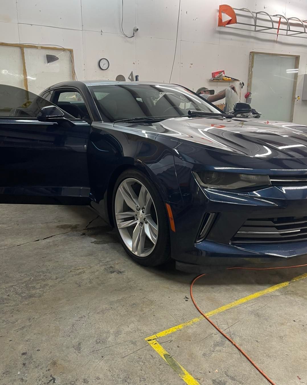 A dark blue Chevrolet Camaro parked inside a garage with its driver-side door open.