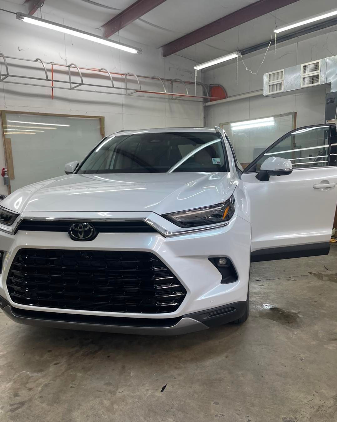 A white Toyota RAV4 parked inside a bright, industrial garage with its driver-side door open.