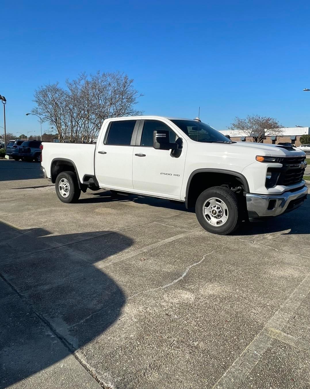 A white Chevrolet Silverado pickup truck parked on a concrete lot under a clear blue sky.