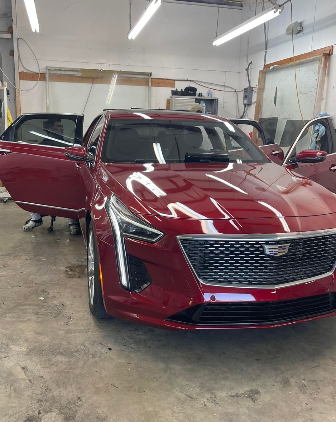 A deep red Cadillac sedan with its front doors open, parked inside a brightly lit garage or workshop.