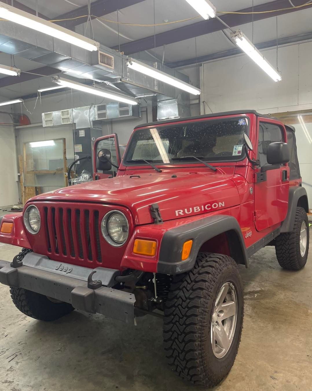 A red Jeep Rubicon parked inside a brightly lit industrial garage.