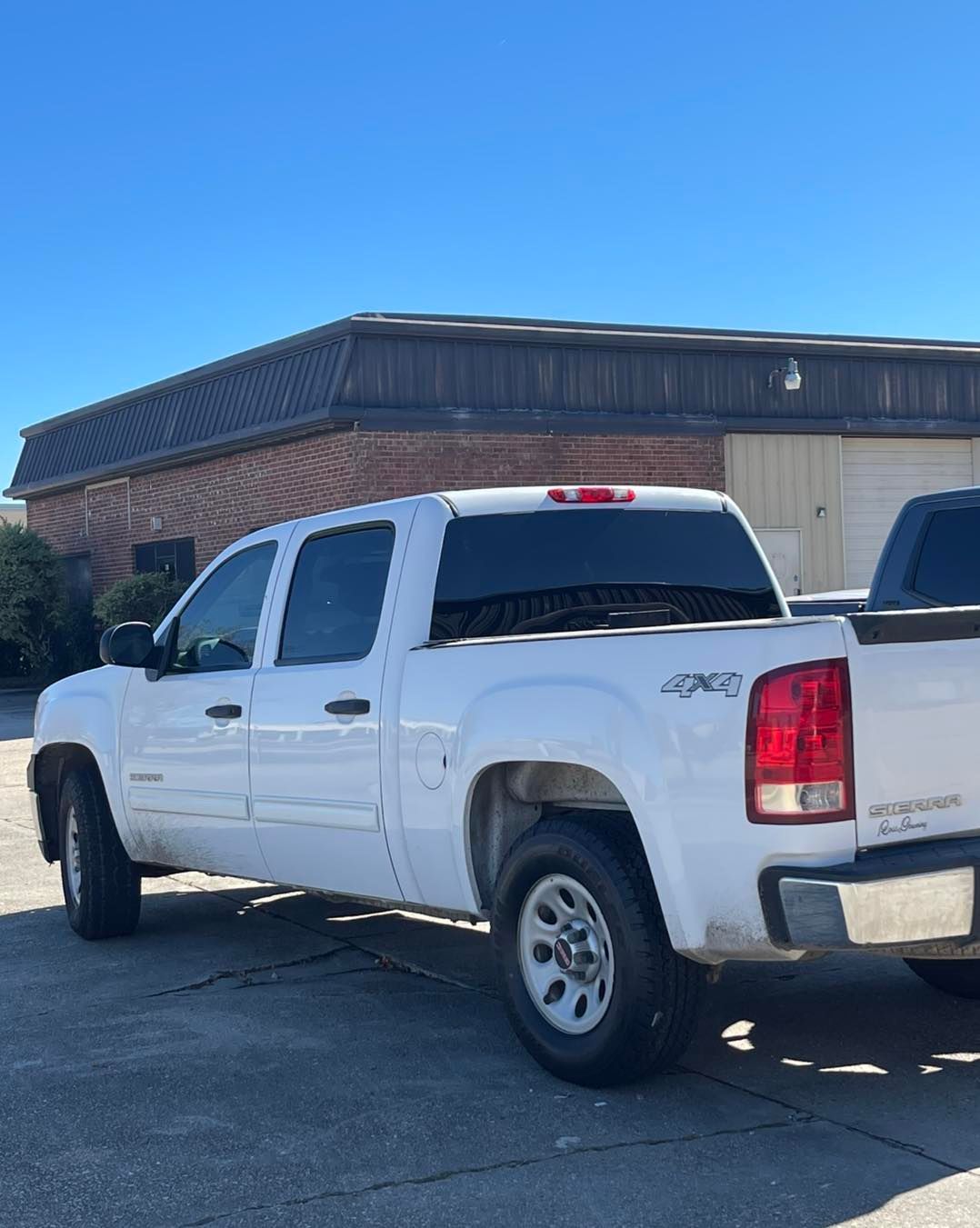 A white GMC Sierra crew cab pickup truck parked on an asphalt lot in front of a brick commercial building.