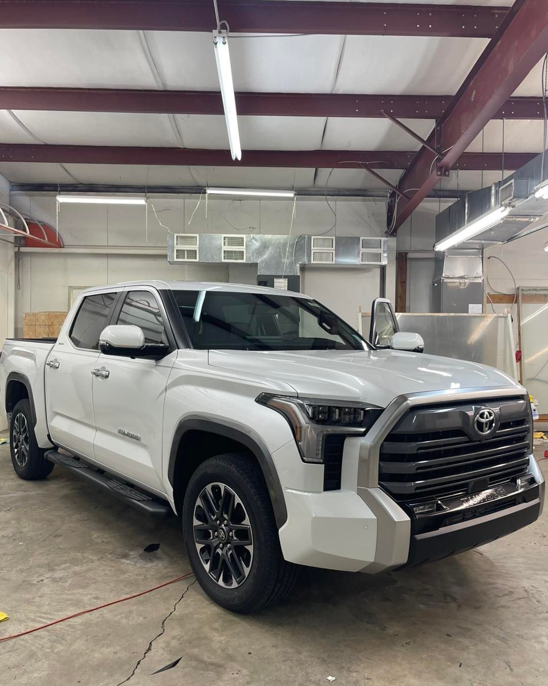 A white Toyota Tundra pickup truck parked in an indoor garage under bright overhead lighting.