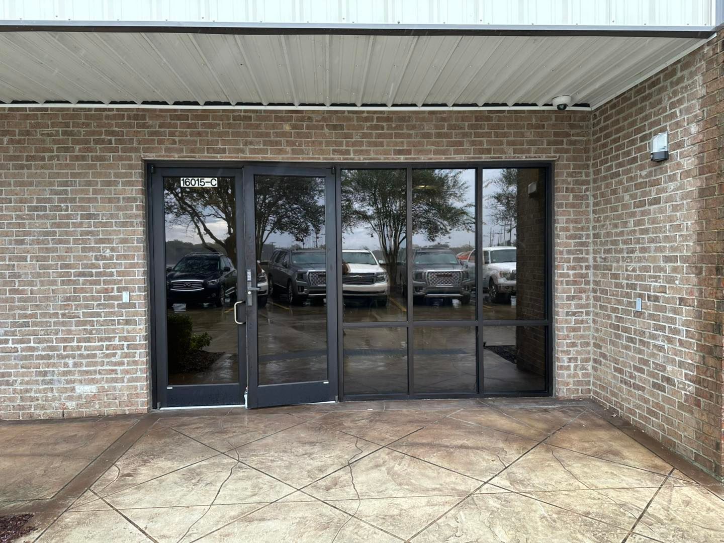 A storefront entrance with a glass door and windows set into a brick exterior wall above a stamped concrete porch.