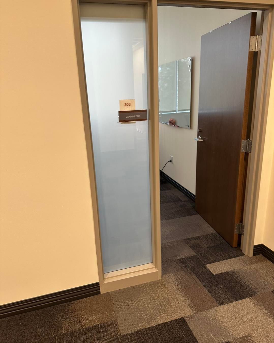 An office doorway with a frosted glass side panel and a brown door partially open, revealing a carpeted room.