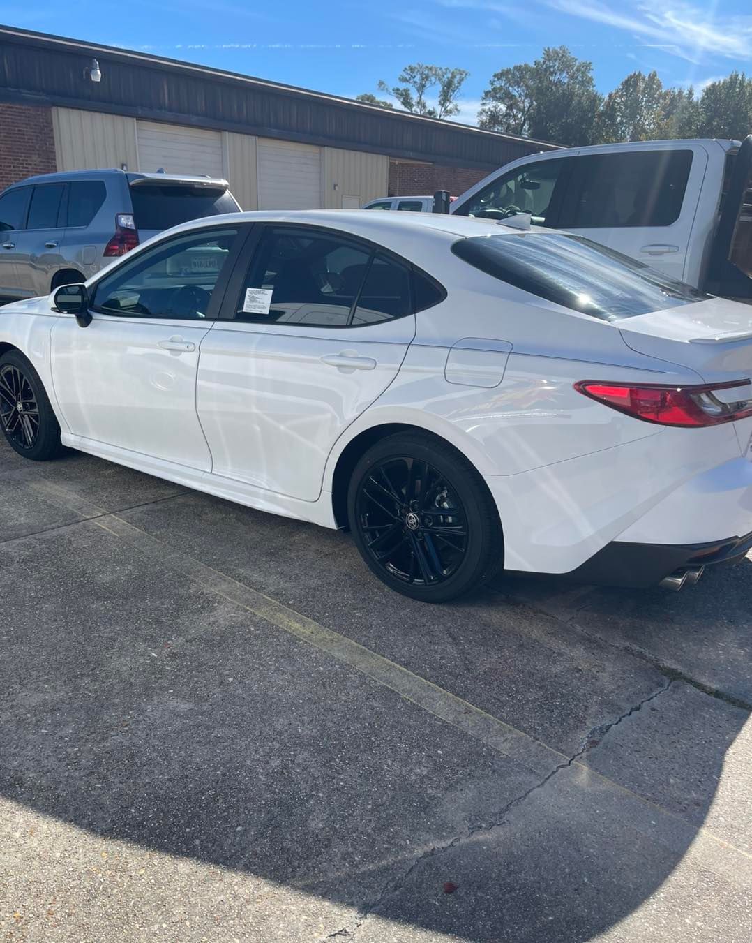 A white Honda sedan with black rims parked in a paved lot on a sunny day.