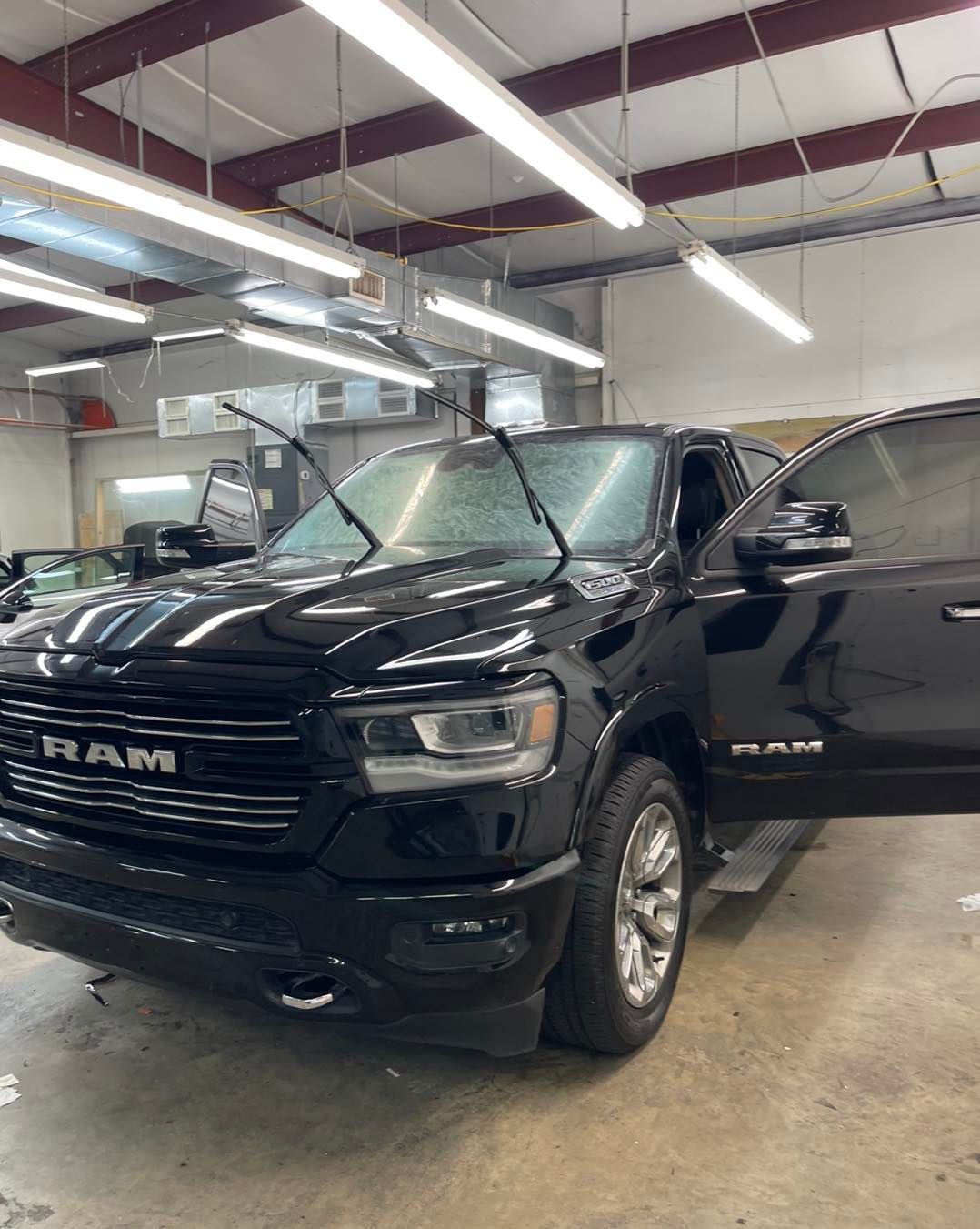 A black RAM pickup truck with a shattered windshield parked inside a brightly lit garage or workshop.