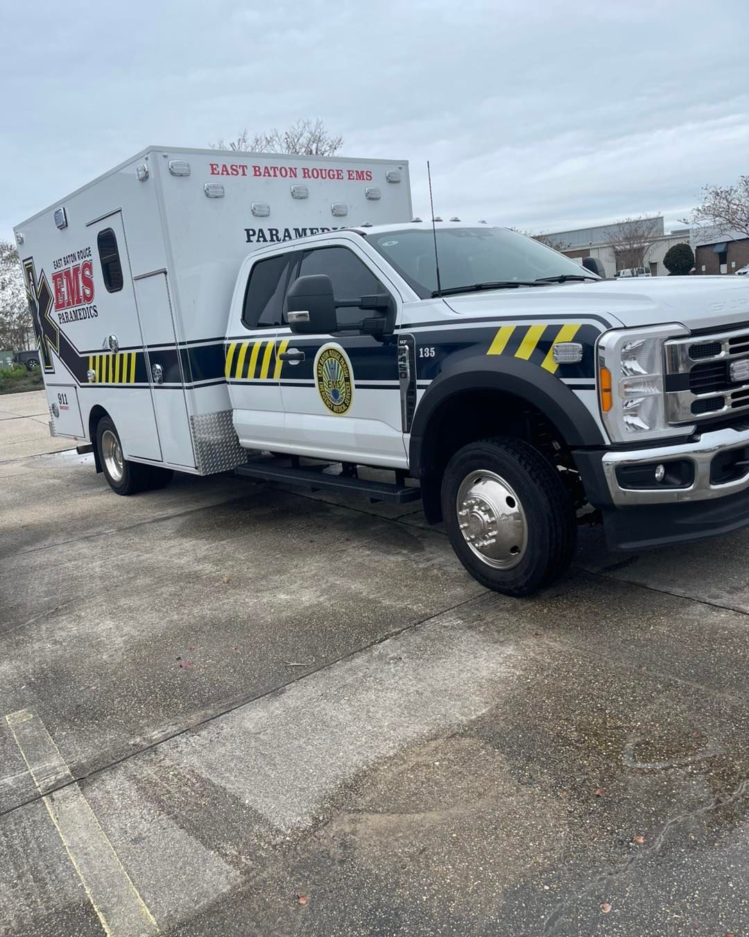 A white Ford ambulance with yellow and black chevron markings on the side, parked outdoors on a paved lot.