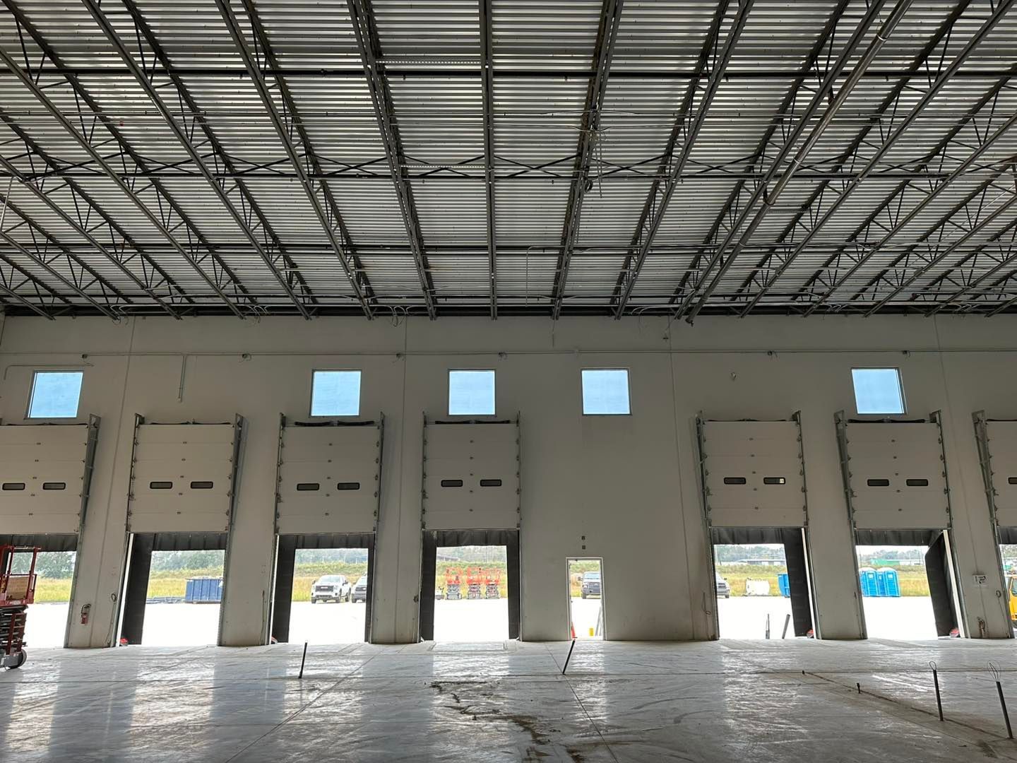 An interior view of a large warehouse featuring several open loading dock bays and high, exposed metal truss ceilings.