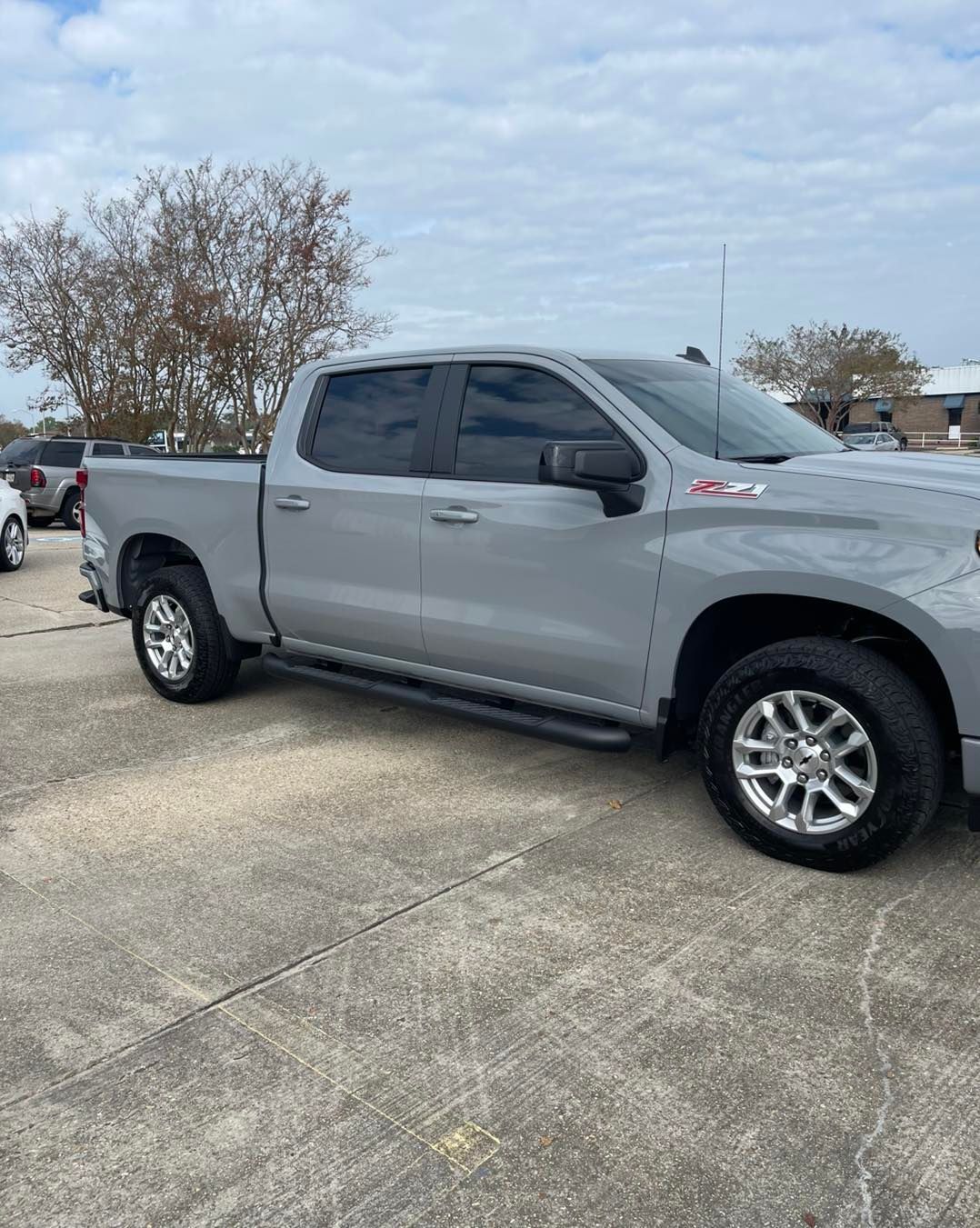 A grey four-door pickup truck parked on an asphalt lot under a cloudy sky.