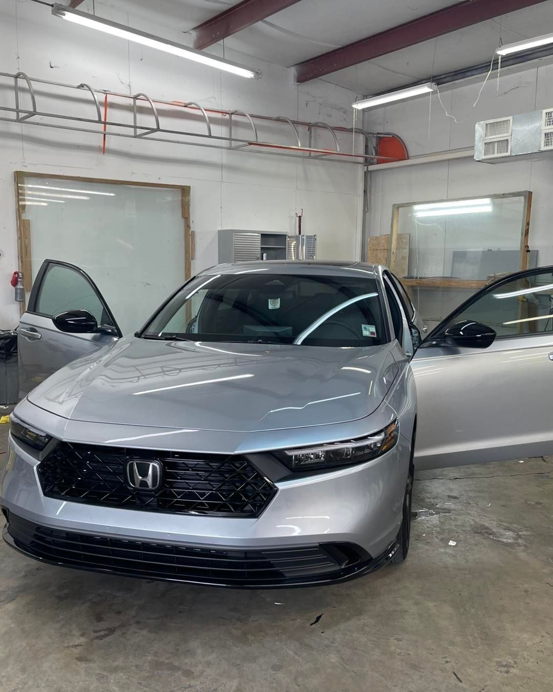 A silver Honda Accord with both front doors open, parked inside a brightly lit auto shop.