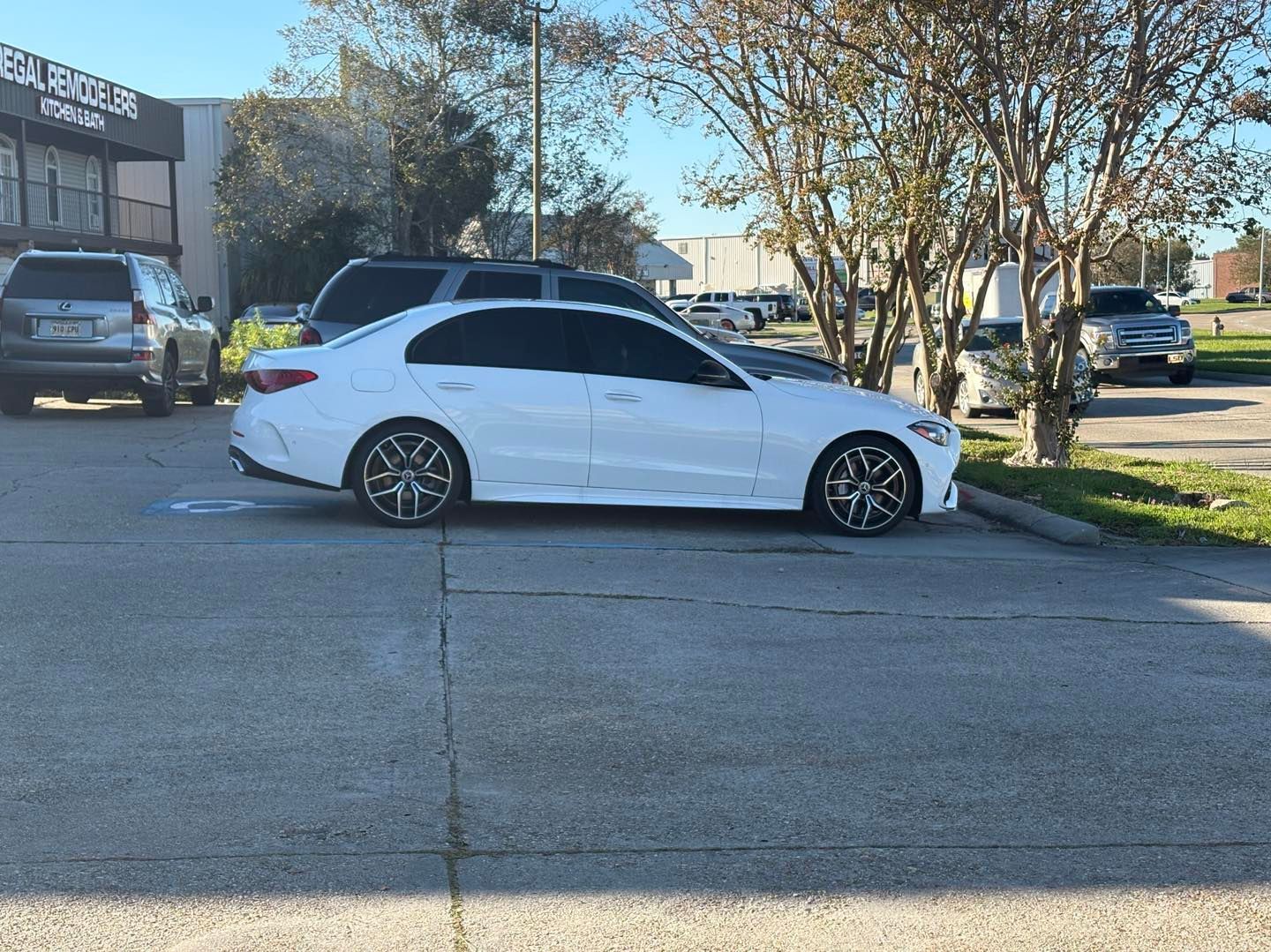 A white sedan parked in an outdoor lot on a sunny day with other vehicles in the background.