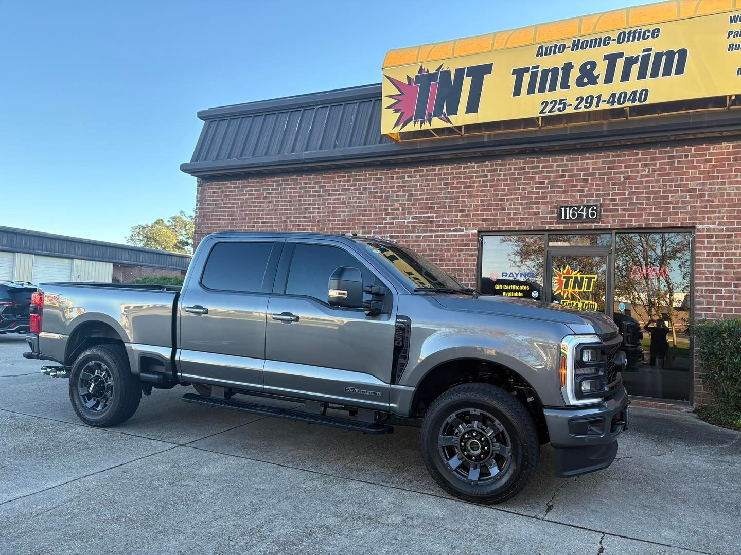 A gray Ford Super Duty pickup truck parked in front of a brick building with a yellow 