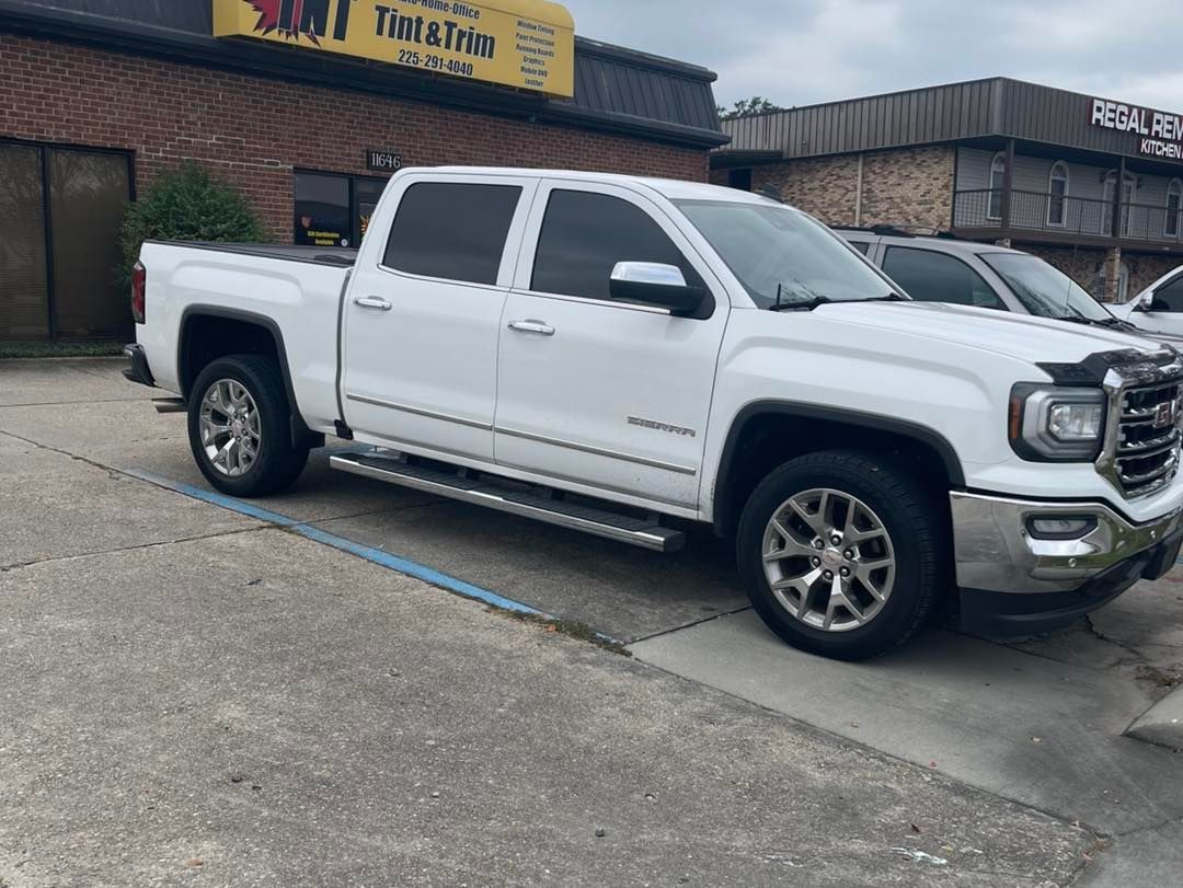 A white GMC pickup truck parked in a paved lot in front of a brick commercial building.