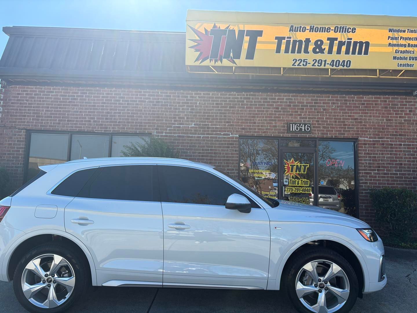 A white Audi SUV parked in front of a brick building with a yellow sign for 