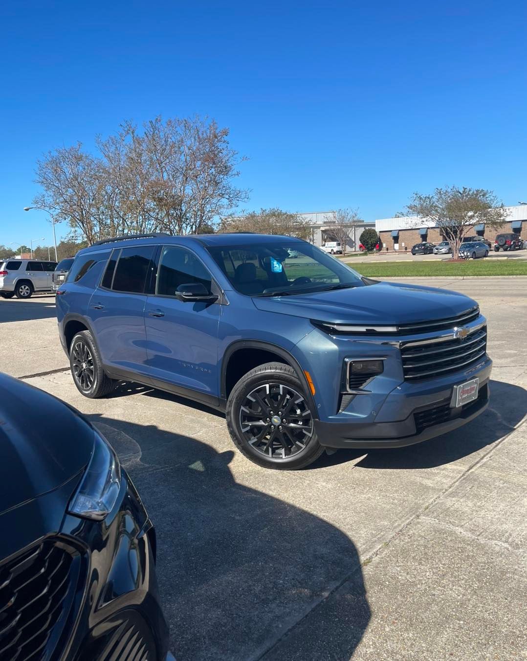 A blue Chevrolet Traverse SUV with black rims parked in a sunlit outdoor lot.
