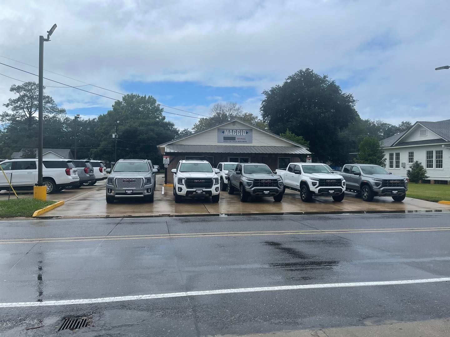 A car dealership lot featuring several white and grey pickup trucks parked in front of a small, single-story office.